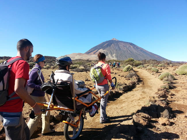 Una persona con movilidad reducida, junto a varios acompañantes, recorre en una joëlette un sendero del Parque Nacional del Teide (foto: FGN).